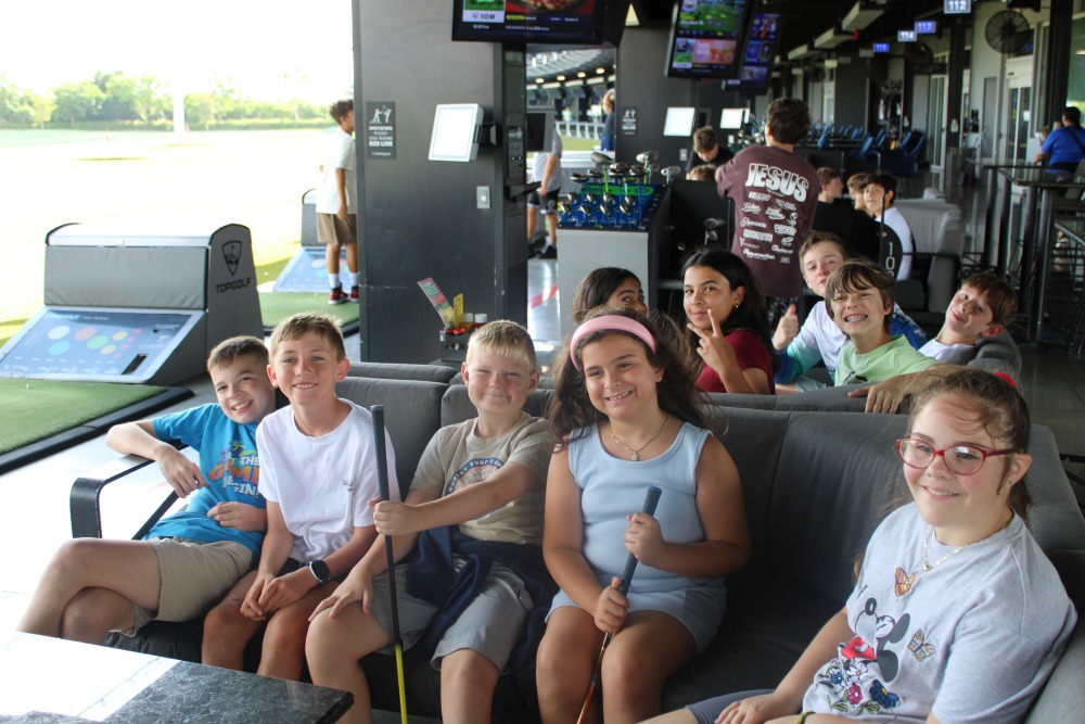 Teen swings a golf club at an outdoor Topgolf bay on a sunny day.